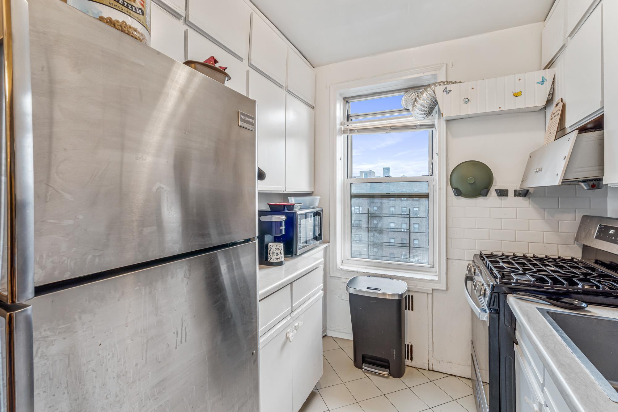 Galley kitchen with white cabinets and stainless steel appliances in a Rego Park, Queens NY co-op for sale at 65-74 Saunders Street 6J — Homes by Agatha