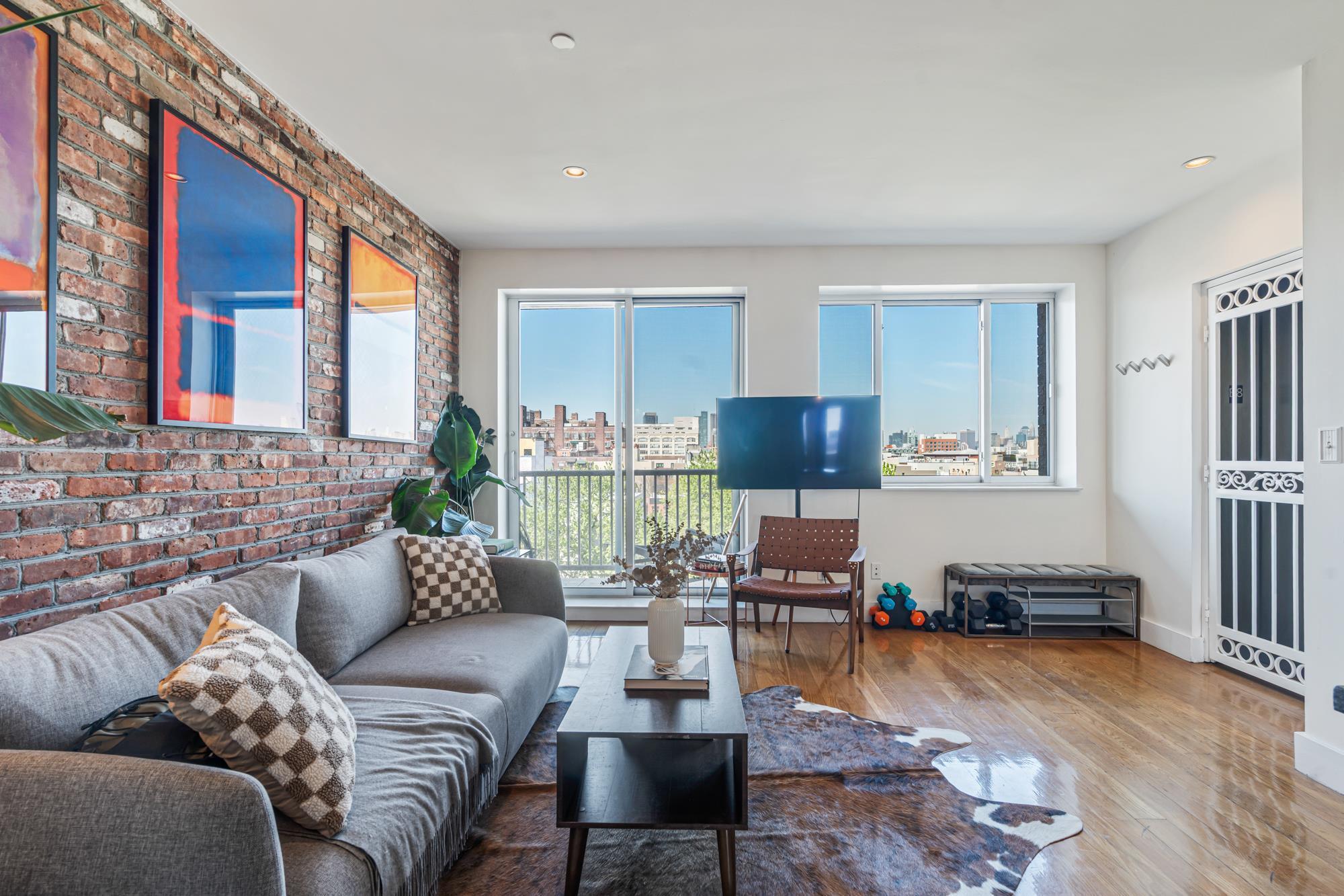 Sunlit living room with exposed brick and skyline views in a Brooklyn, NY condo for sale at 197 Spencer Street #8B — Homes by Agatha